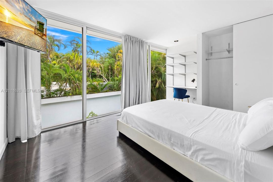 Floor-to-ceiling sliding glass doors, wood-finish flooring, built-in shelving, and integrated closet with hanging rod