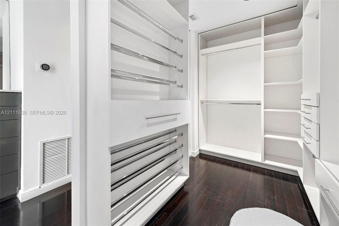 Custom walk-in closet featuring white built-in shelving, integrated chrome hanging rods, stacked storage drawers, and dark wood-finish flooring