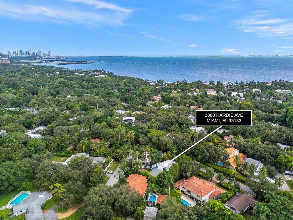 Aerial perspective featuring a two-story residence with a clay tile roof, private swimming pool, mature tree canopy, and coastal proximity