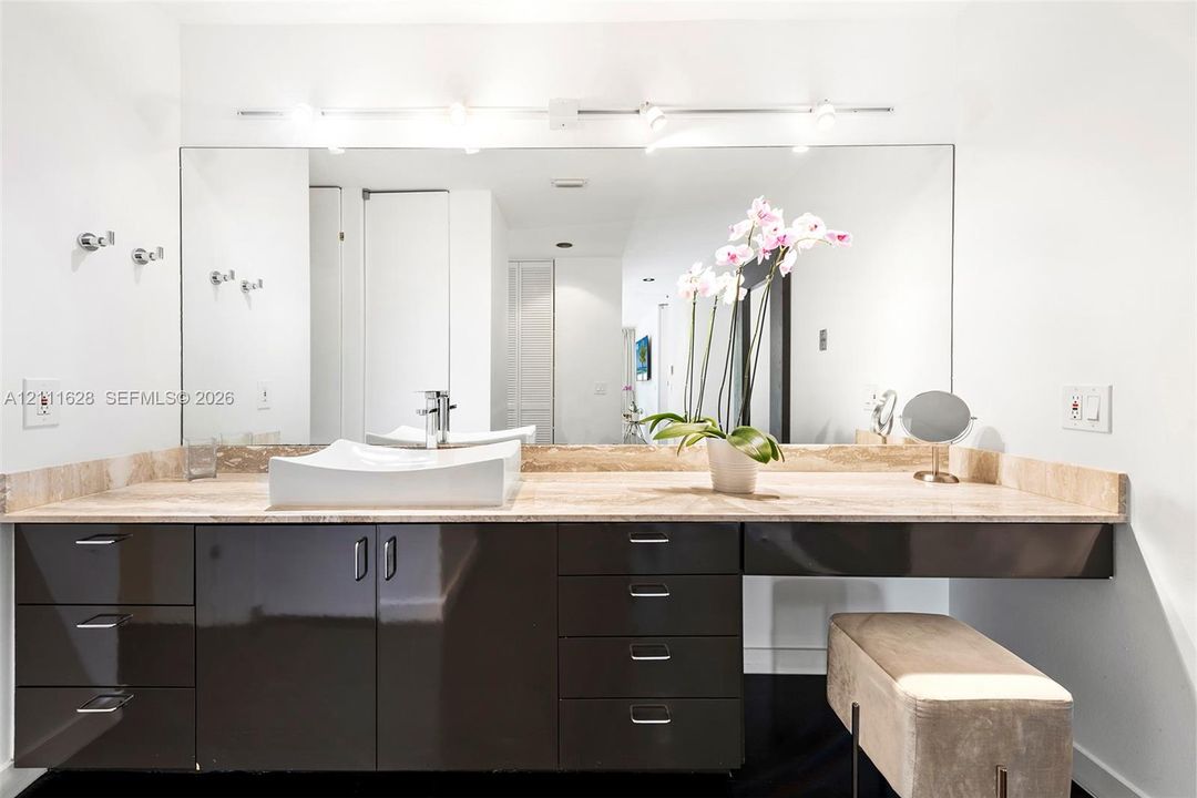 Dark cabinetry vanity featuring a stone countertop, integrated vessel sink, track lighting, and a full-width wall mirror