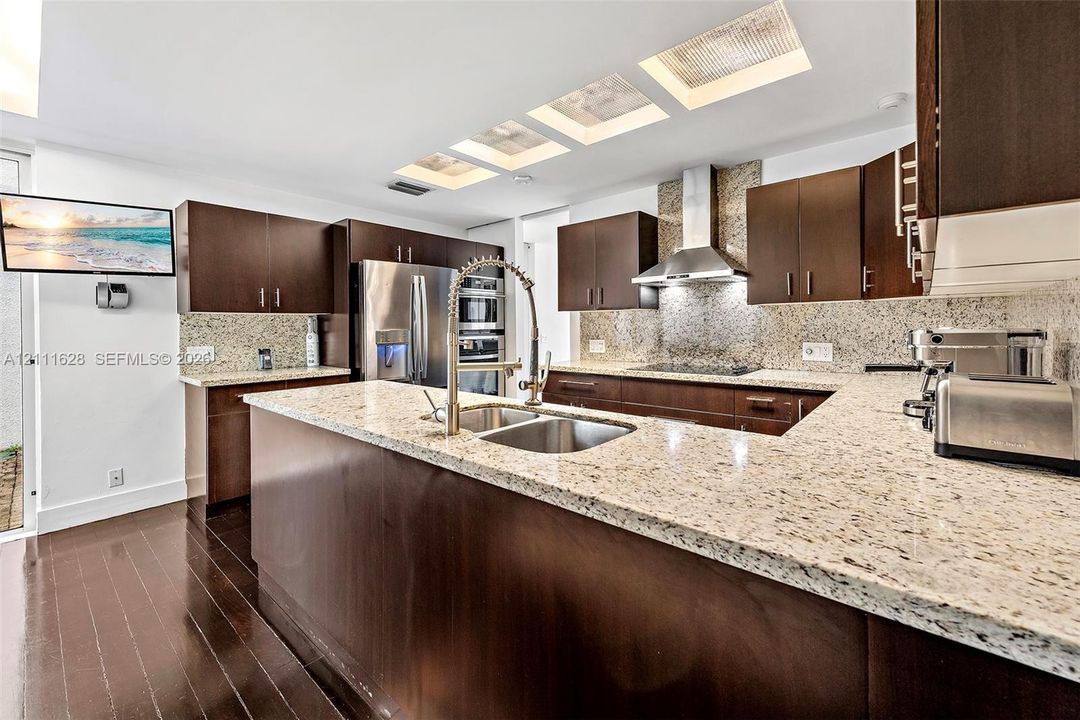 Kitchen featuring dark wood-finish cabinetry, stone-style countertops, stainless steel appliances, recessed ceiling lighting, and wood-finish flooring