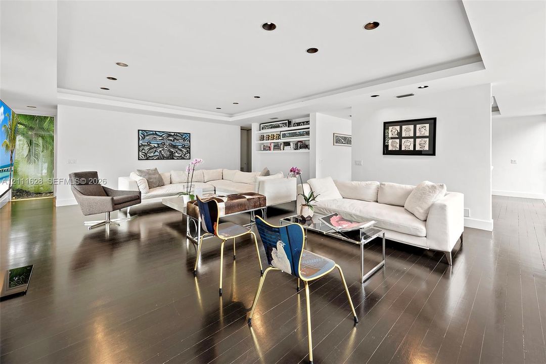 Spacious interior featuring dark wood-finish flooring, tray ceilings with recessed lighting, built-in shelving, and large floor-to-ceiling windows