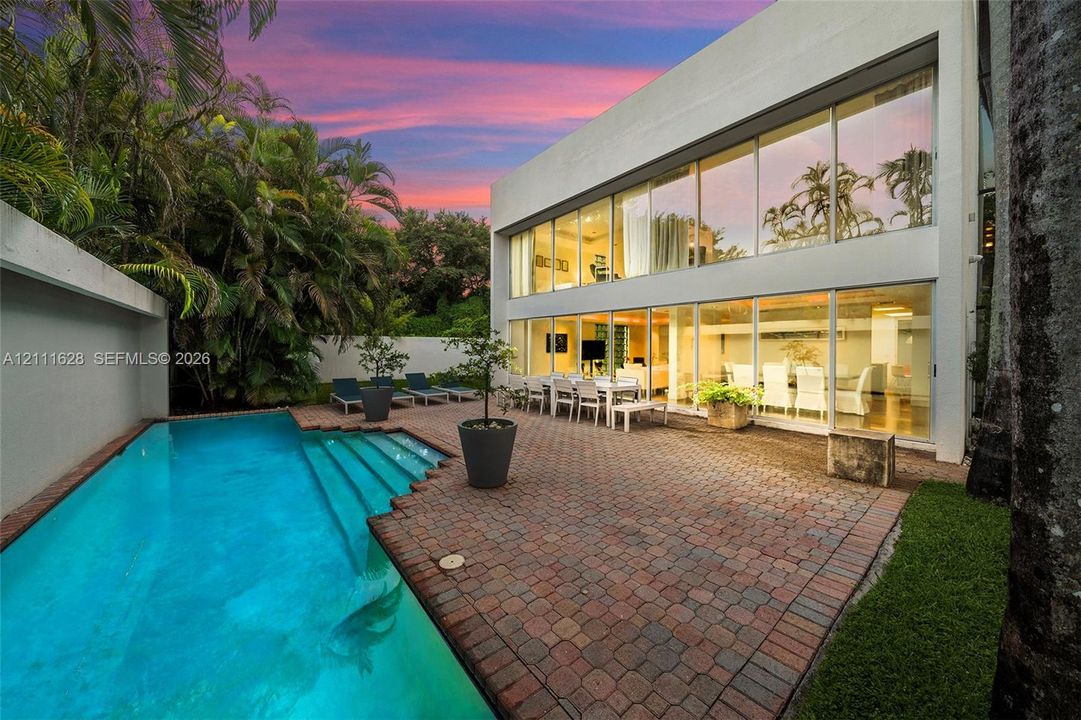 Contemporary two-story exterior with floor-to-ceiling glass walls, paver patio, and in-ground swimming pool