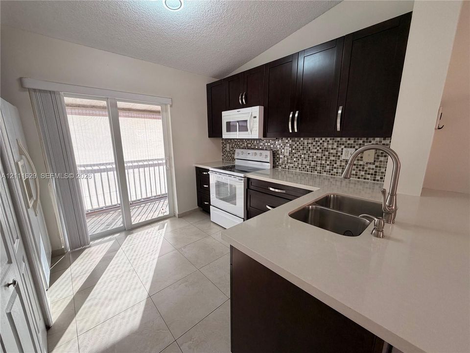 Kitchen featuring dark cabinetry, quartz countertops, a mosaic tile backsplash, a dual-basin stainless steel sink with a high-arch faucet, and porcelain tile flooring