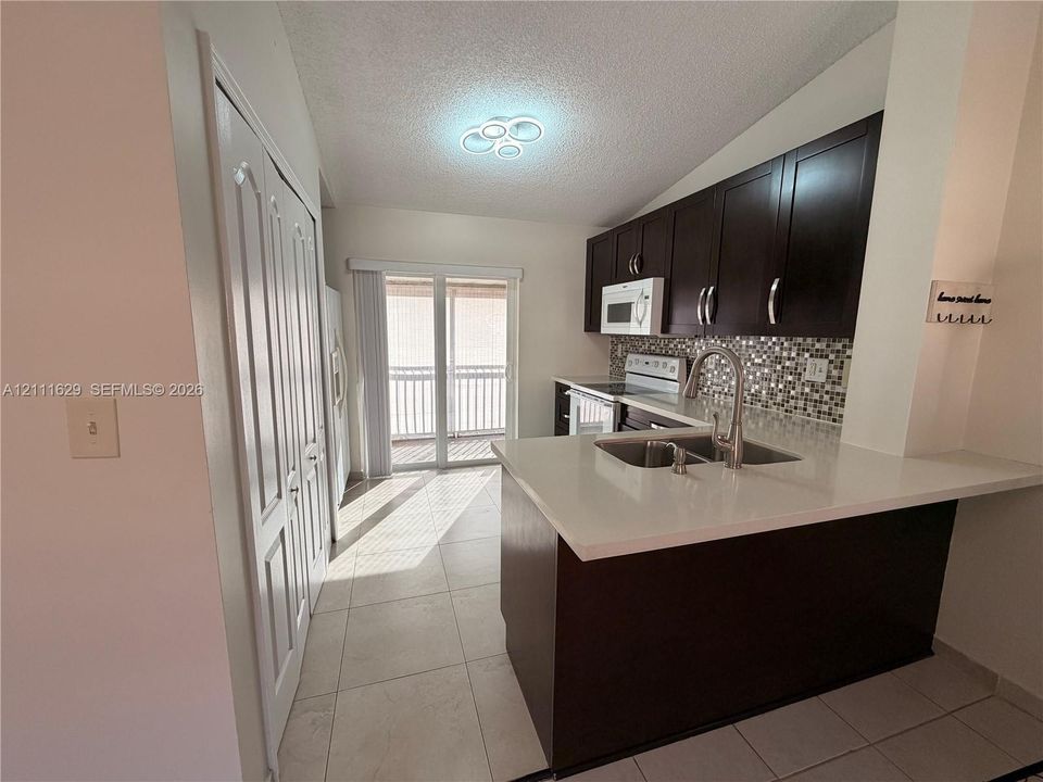 Kitchen featuring dark cabinetry, quartz countertops, mosaic tile backsplash, double-basin stainless steel sink with pull-down faucet, and tile flooring