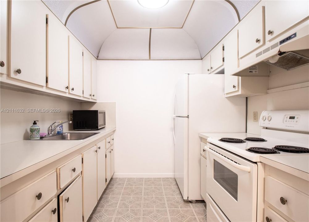 Galley kitchen featuring white cabinetry, solid-surface countertops, vaulted ceiling, and built-in white appliances