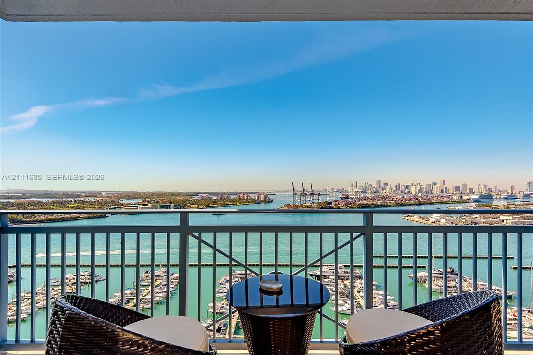 Covered balcony with metallic railing overlooking a marina and distant urban skyline