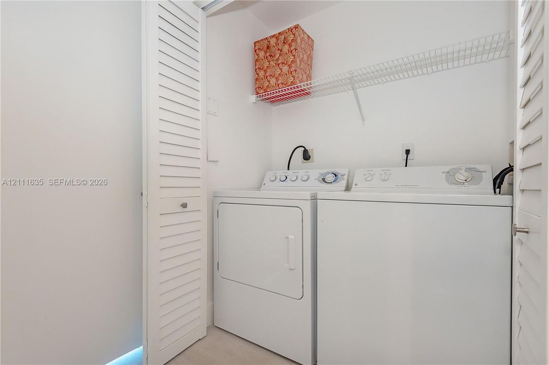 Laundry closet featuring white louvered doors, wire shelving, and dedicated hookups for a washer and dryer