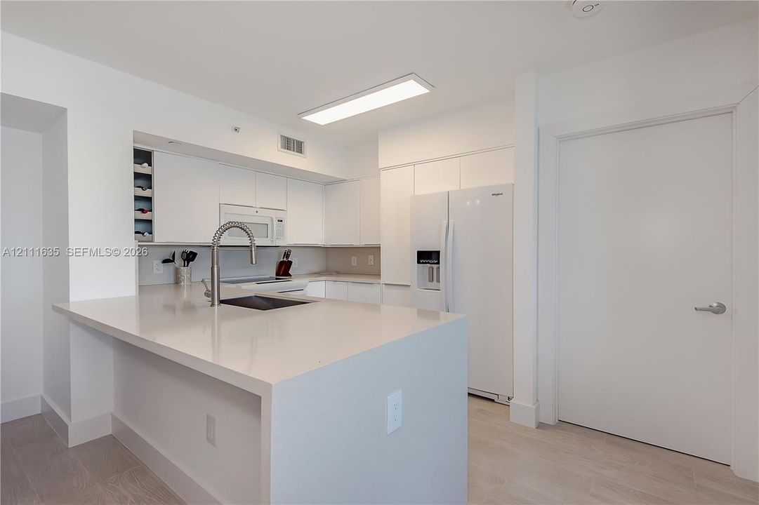 Kitchen featuring flat-panel white cabinetry, solid surface countertops, built-in wine rack, integrated microwave, and wood-finish flooring