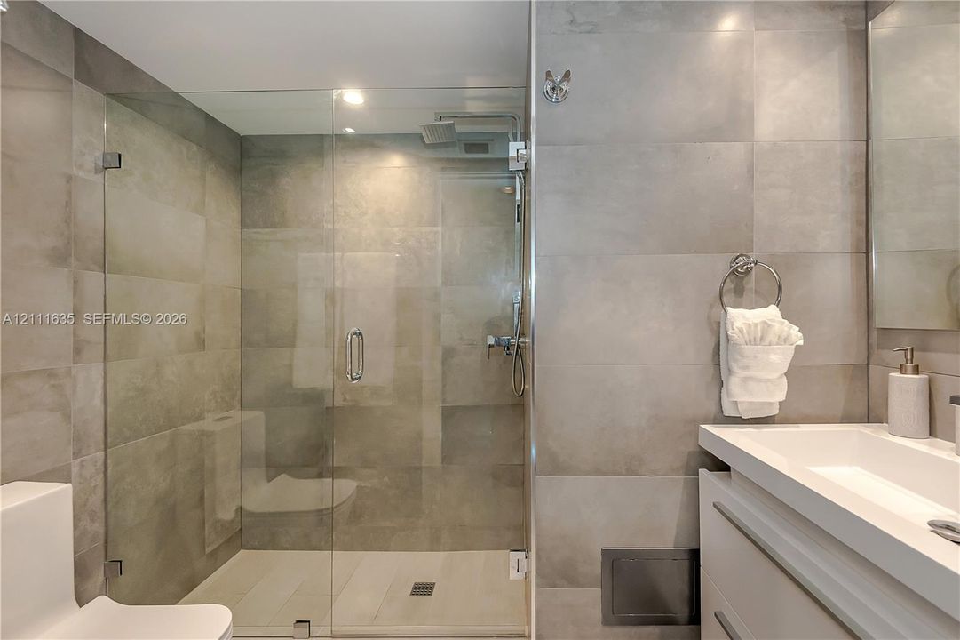 Walk-in glass-enclosed shower featuring large-format gray wall tiling, rainfall showerhead, floating vanity with integrated rectangular sink, and polished chrome fixtures