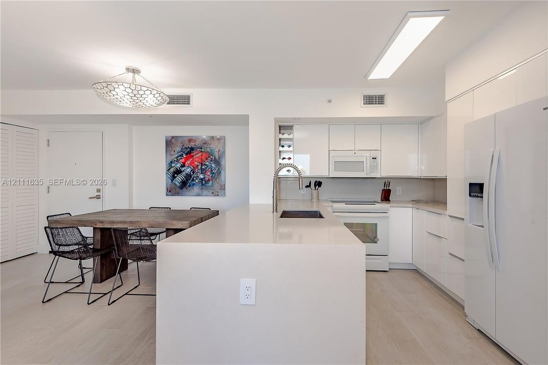 Kitchen featuring white slab cabinetry, an oversized quartz waterfall island, built-in wine storage, light-toned wood-finish flooring, and a modern geometric pendant light fixture