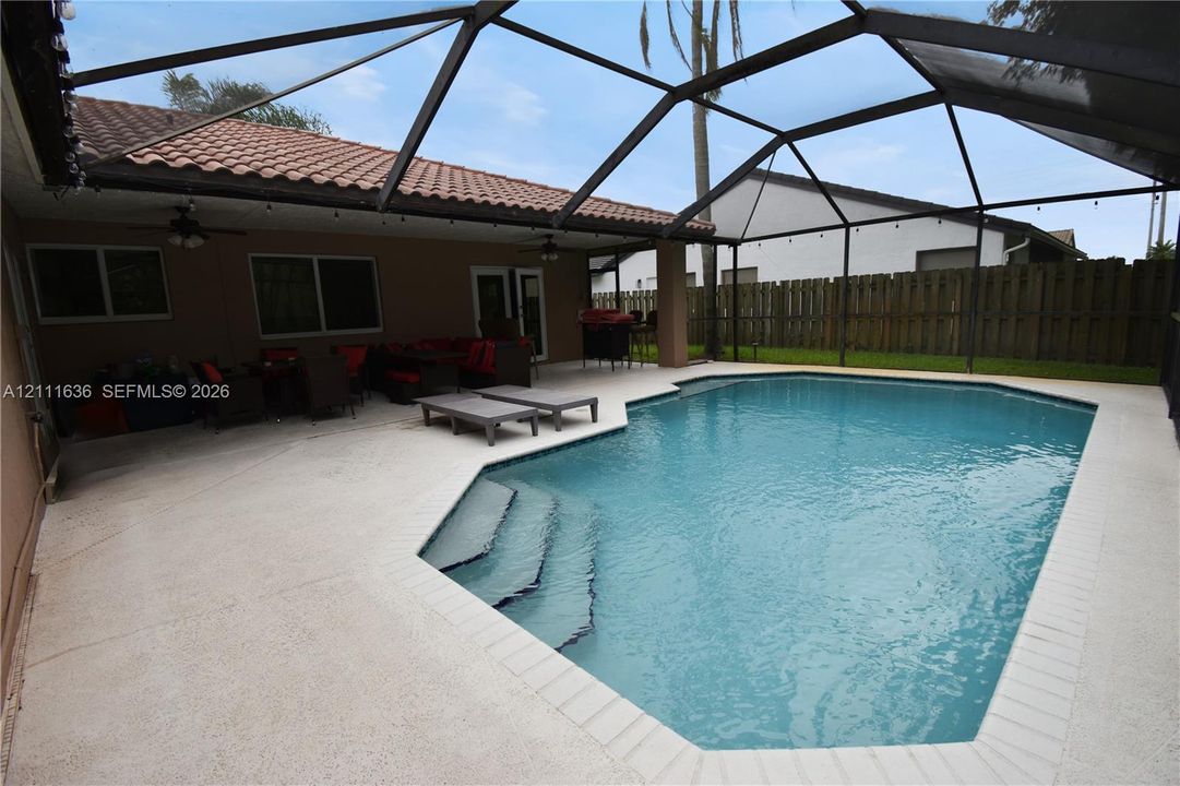 Screened-in lanai featuring a swimming pool with integrated stairs, expansive concrete decking, tile roof, and two ceiling fans