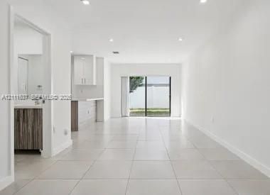 Large-format tile flooring, recessed ceiling lighting, sliding glass door, and cabinetry featuring light-toned countertops