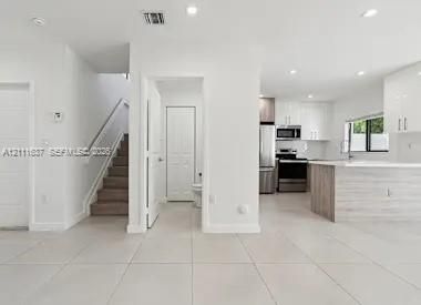 Open-concept floor plan featuring large-format ceramic tile flooring, kitchen with high-gloss cabinetry, stainless steel appliances, and a wood-finish kitchen island