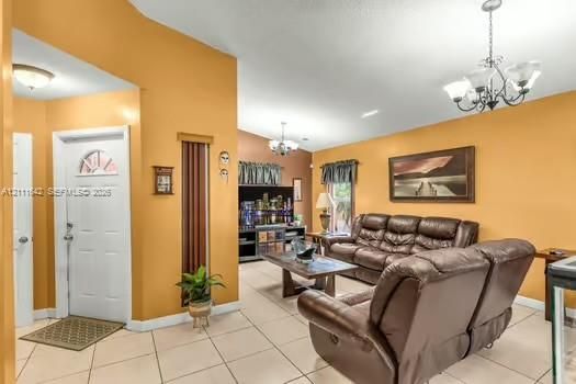 Entryway featuring high ceilings, light-colored tile flooring, decorative chandeliers, and a white six-panel door with arched glass inlay
