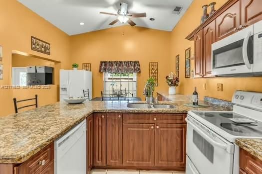 Kitchen featuring a vaulted ceiling, stained wood cabinetry, stone-finish countertops, stainless steel dual-basin sink, and recessed lighting