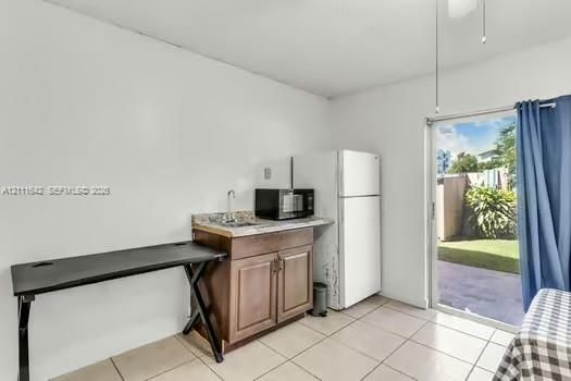 Kitchenette featuring wood-finish cabinetry, stone-texture countertop, inset sink, and tile flooring, with sliding glass door access to an exterior patio