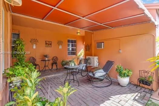 Covered patio featuring brick pavers, a metal frame overhead structure, and wall-mounted exterior lighting