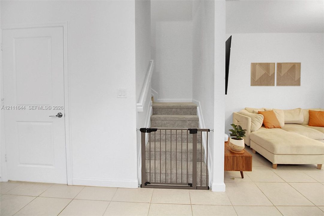 Neutral-toned ceramic tile flooring, staircase with carpeted treads, and painted white interior doors with satin nickel hardware