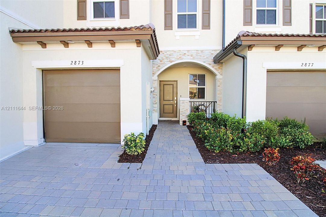 Exterior featuring a paver driveway, single-car garage, stone veneer entryway accents, and a covered portico with arched detailing