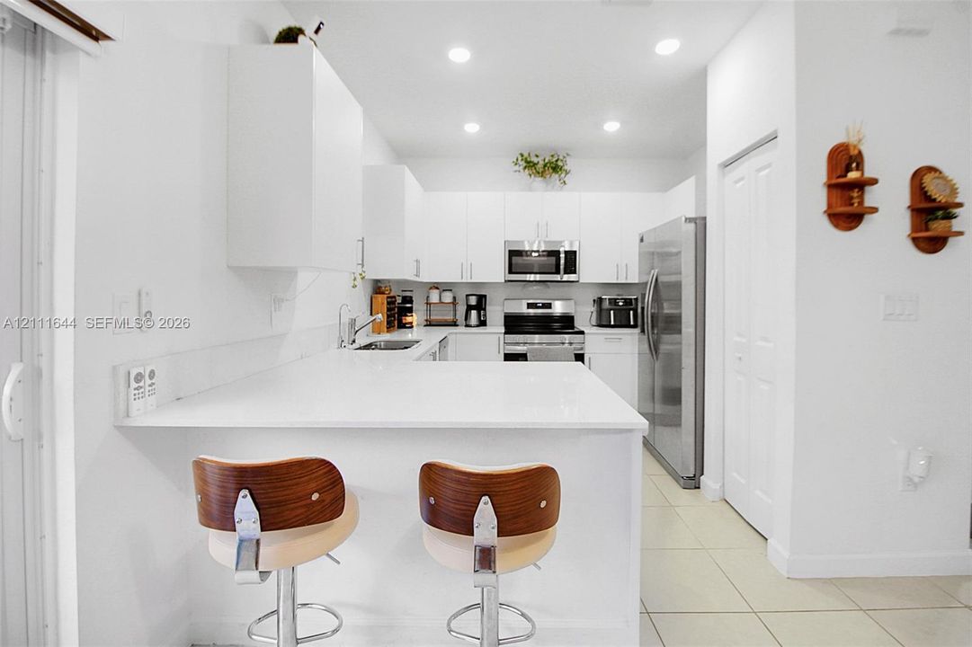 Kitchen featuring white cabinetry, solid-surface countertops with a breakfast bar, recessed ceiling lighting, and stainless-steel appliances