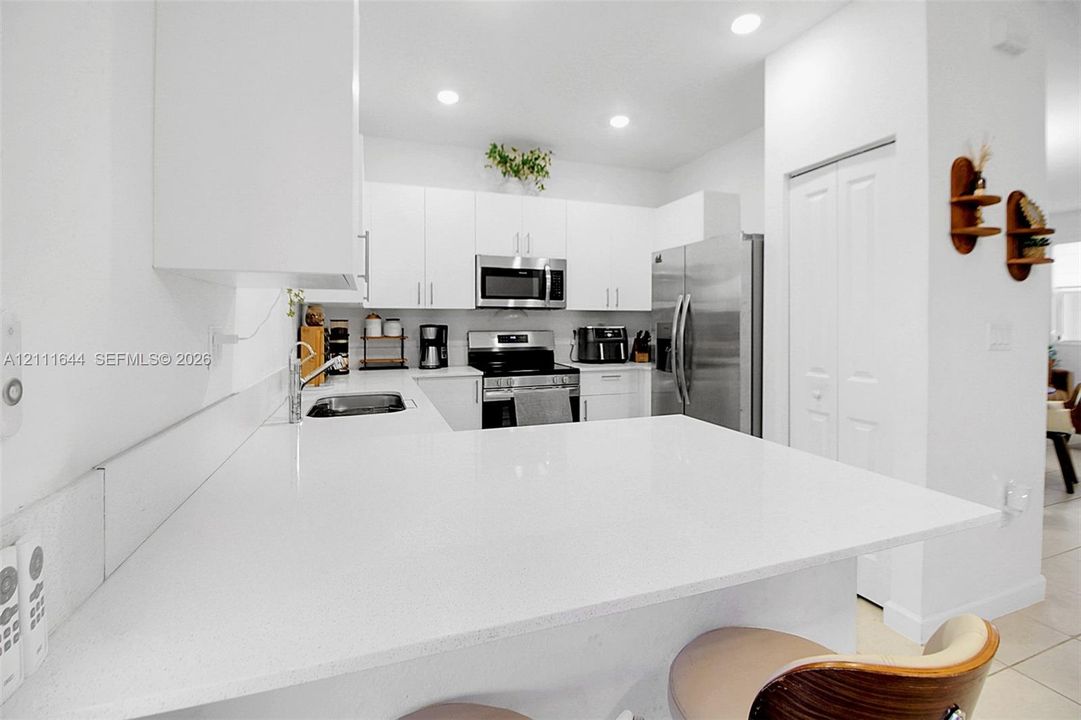 Kitchen featuring white shaker-style cabinetry, a solid-surface breakfast bar, stainless steel appliances, and recessed lighting
