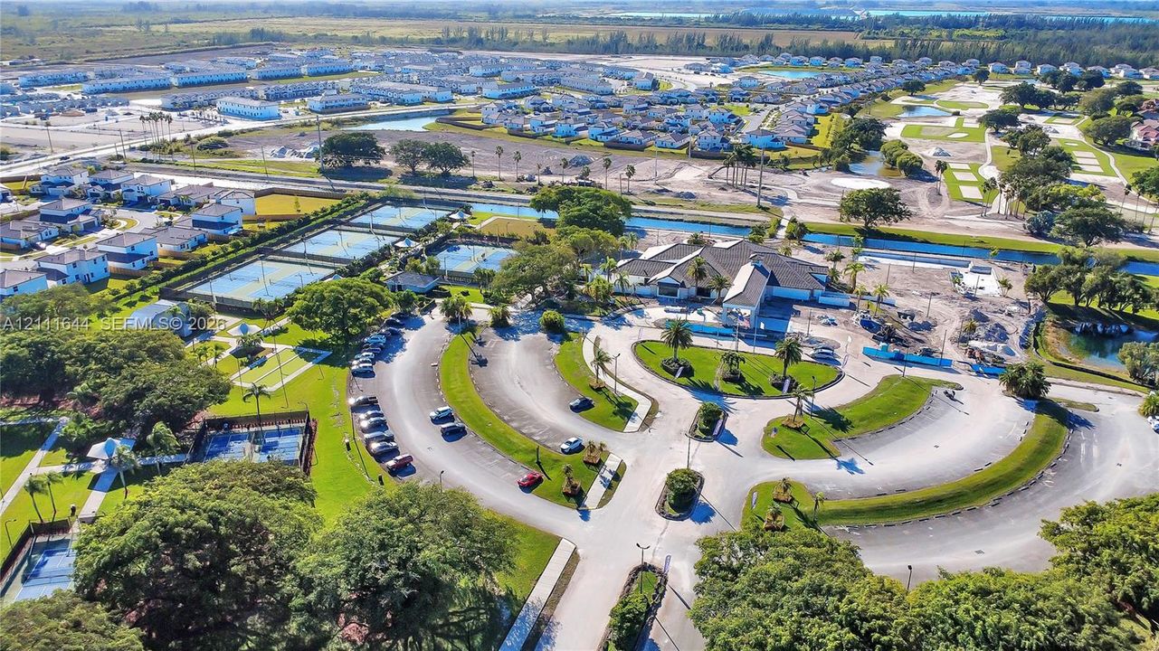 Aerial perspective of community recreational facilities featuring multiple tennis courts, a central clubhouse, an outdoor swimming pool, and landscaped green spaces with mature trees