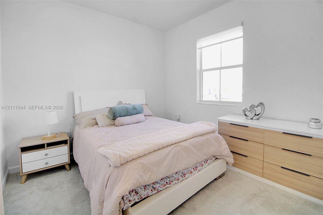 Neutral-toned interior space featuring light-colored wall-to-wall carpeting and a single-pane window with a roller shade