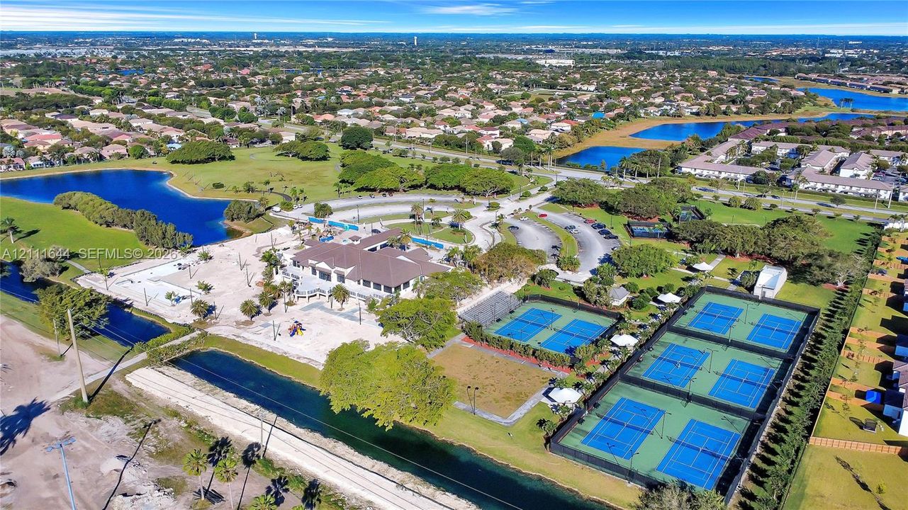 Aerial perspective of a multi-facility recreational complex featuring multiple tennis courts, a central clubhouse, and integrated water features