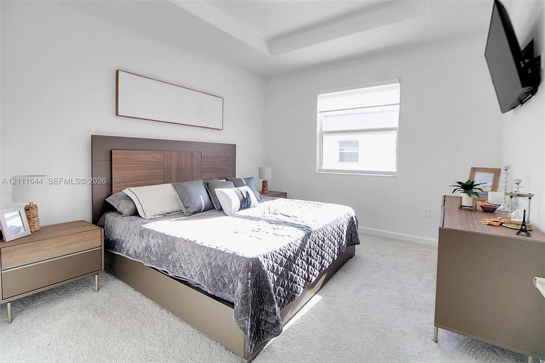 Bedroom featuring neutral wall-to-wall carpeting, tray ceiling, and a single window with roller shade