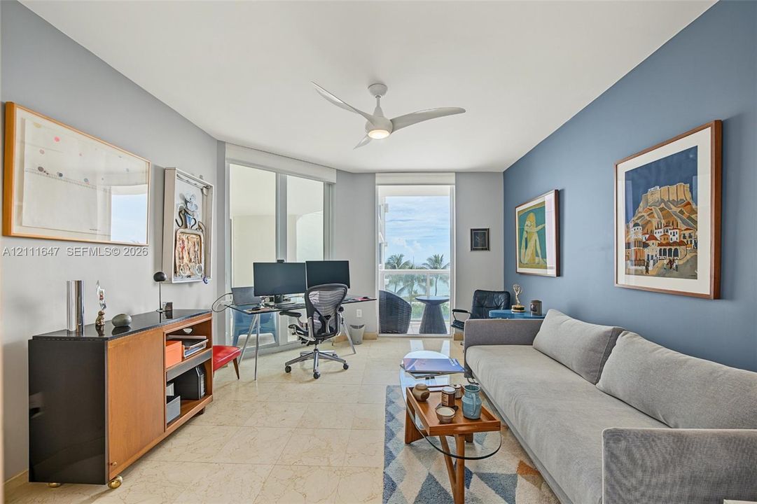 Neutral-toned tile flooring, three-blade ceiling fan with integrated lighting, dual glass-paneled entryways, and floor-to-ceiling glass wall panels