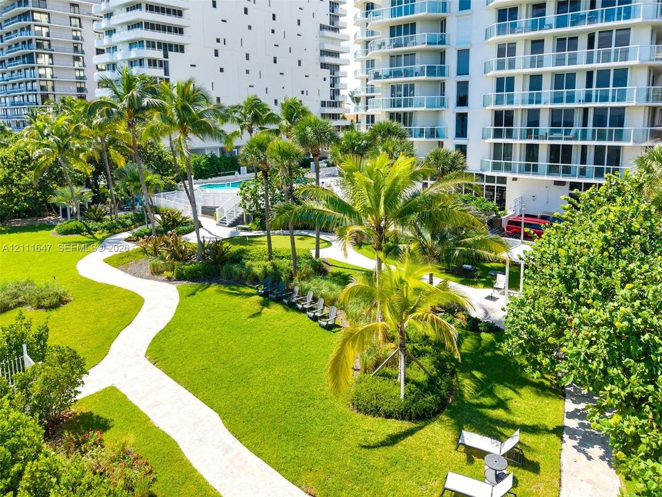 Expansive landscaped grounds featuring winding paved pathways, mature palm trees, manicured lawns, and a swimming pool