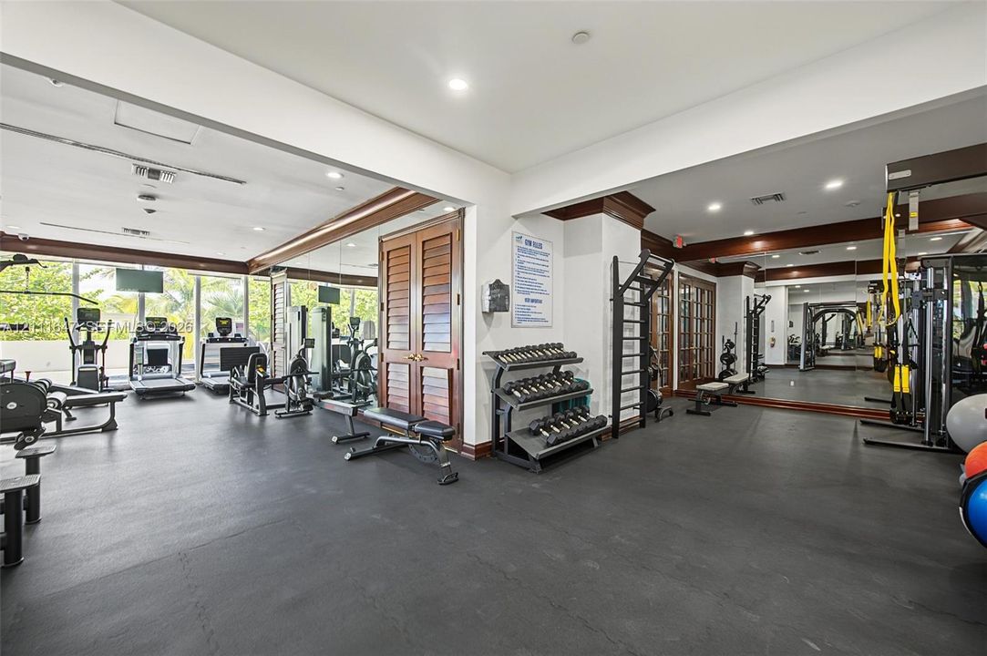 Fitness center featuring high-impact rubber flooring, expansive wall-to-wall mirrors, recessed lighting, and wood-finish louvered door detailing