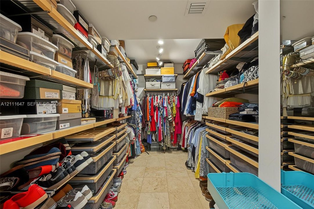 Walk-in closet featuring extensive custom wood shelving, integrated hanging rods, recessed ceiling lighting, and stone flooring