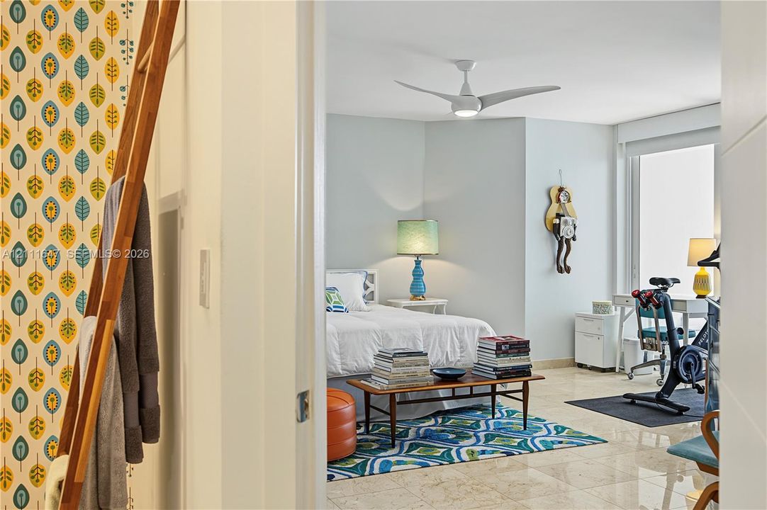 Polished stone flooring, floor-to-ceiling windows, white-finish ceiling fan with integrated lighting, and accent wall featuring a patterned leaf motif