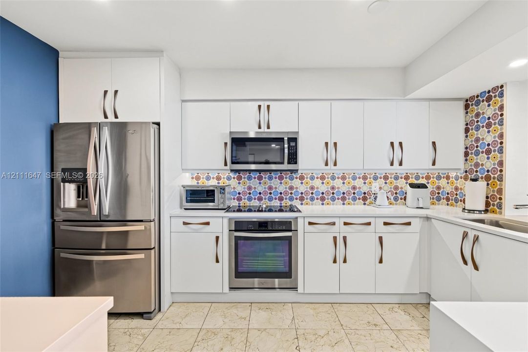 Kitchen featuring white cabinetry, stainless steel appliances, patterned tile backsplash, and stone-finish tile flooring