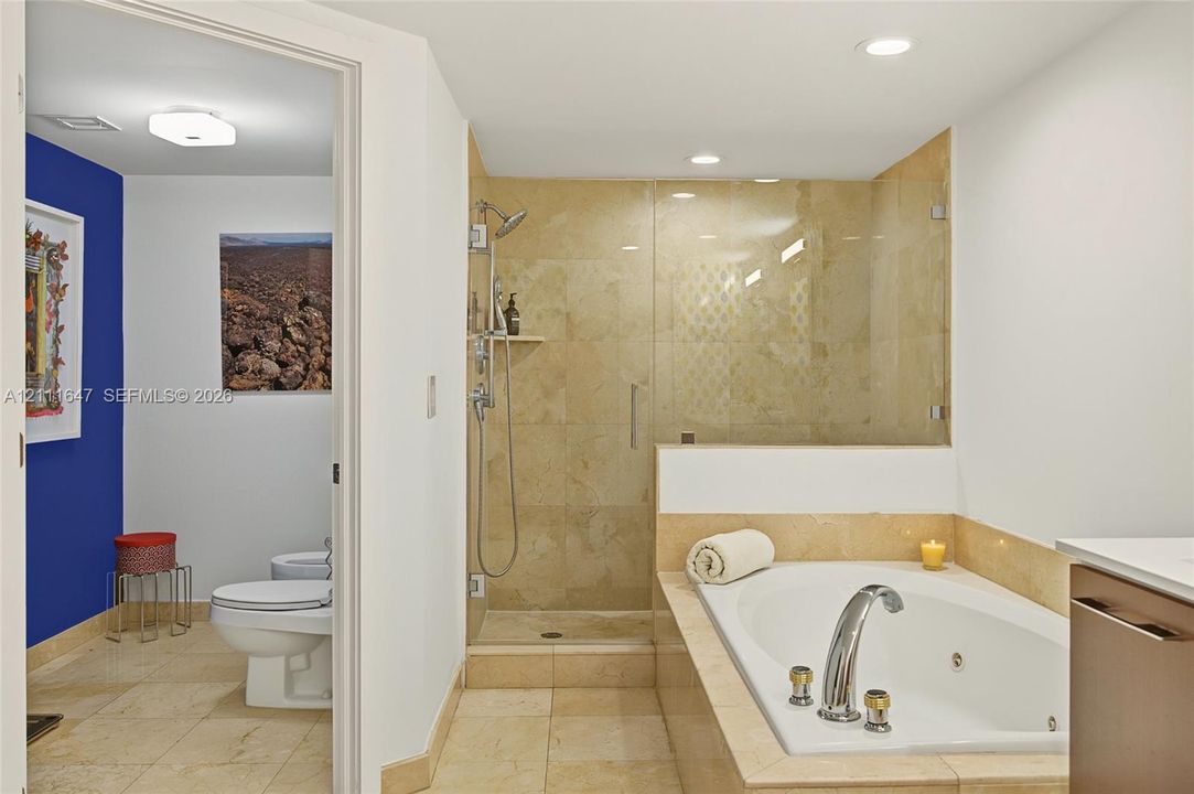 Walk-in shower with natural stone tiling and glass enclosure, integrated jetted soaking tub with stone surround, and tile flooring