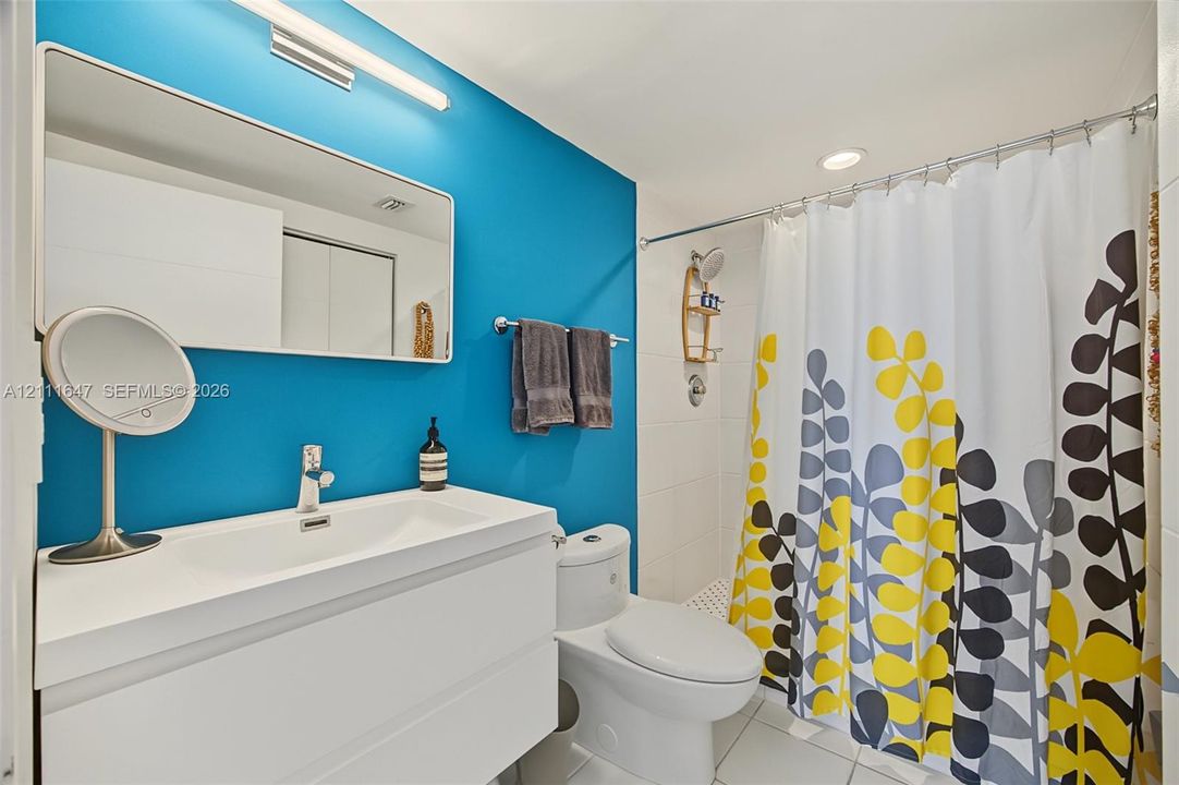 Wall-mounted rectangular mirror, white floating vanity with integrated sink, polished chrome single-handle faucet, and tiled shower surround