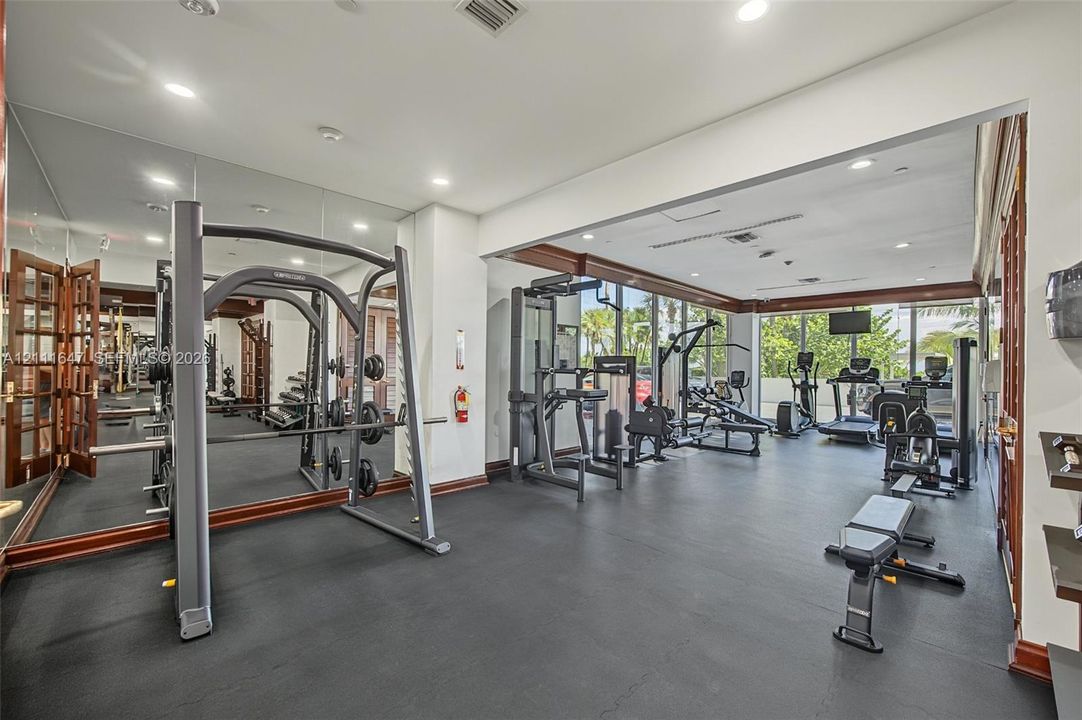 Fitness room featuring wall-to-wall mirrors, expansive floor-to-ceiling windows, recessed lighting, and durable rubber flooring with dark wood-finish trim