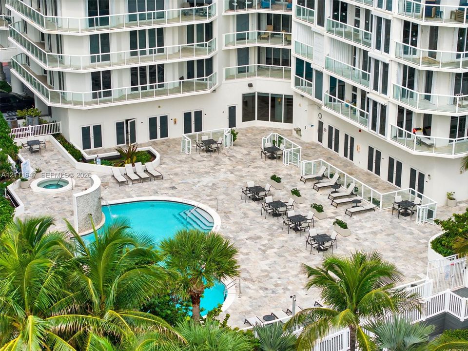Outdoor common area featuring a swimming pool, integrated spa, waterfall feature, and stone-finish decking surrounded by palm trees