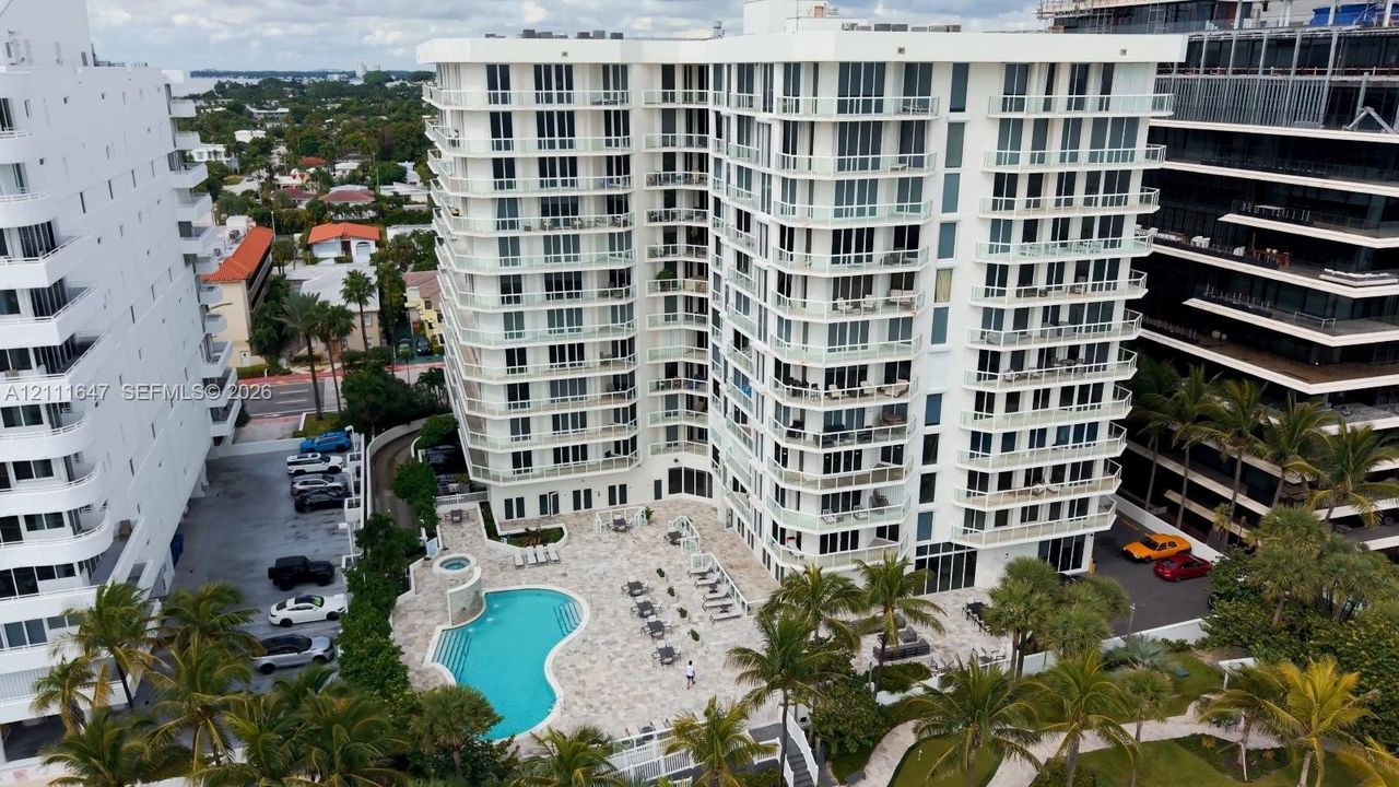 High-rise residential building featuring private balconies, an outdoor swimming pool, stone-paved patio, and mature palm trees
