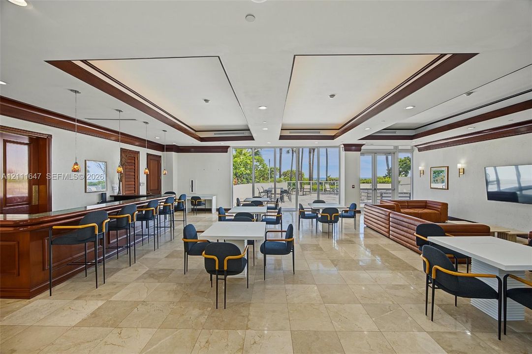 Open-concept common area featuring stone tile flooring, a built-in bar with wood cabinetry, recessed tray ceilin