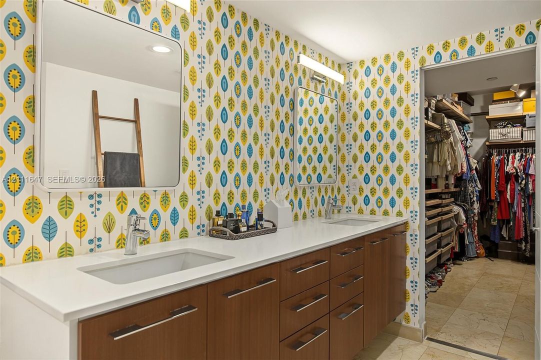 Dual-vanity cabinetry with wood-finish drawer fronts, rectangular undermount sinks, stone countertops, and wall-mounted light fixtures
