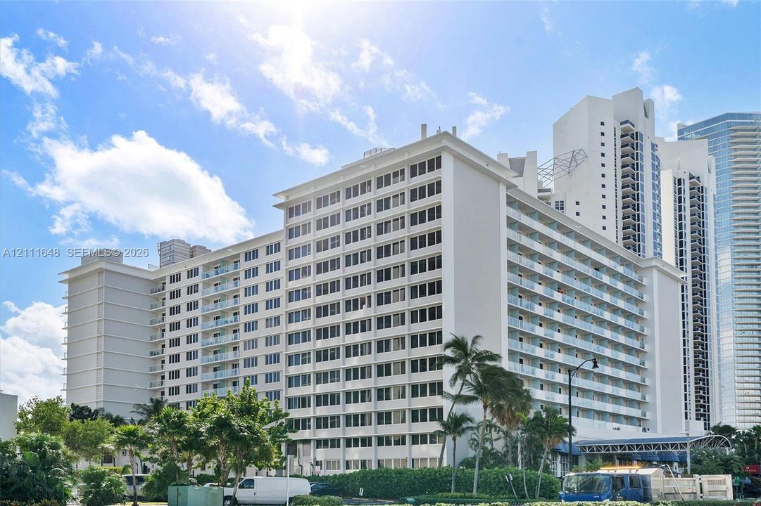 High-rise multi-story exterior featuring white stucco facade, expansive glass-railed balconies, and mature landscaping