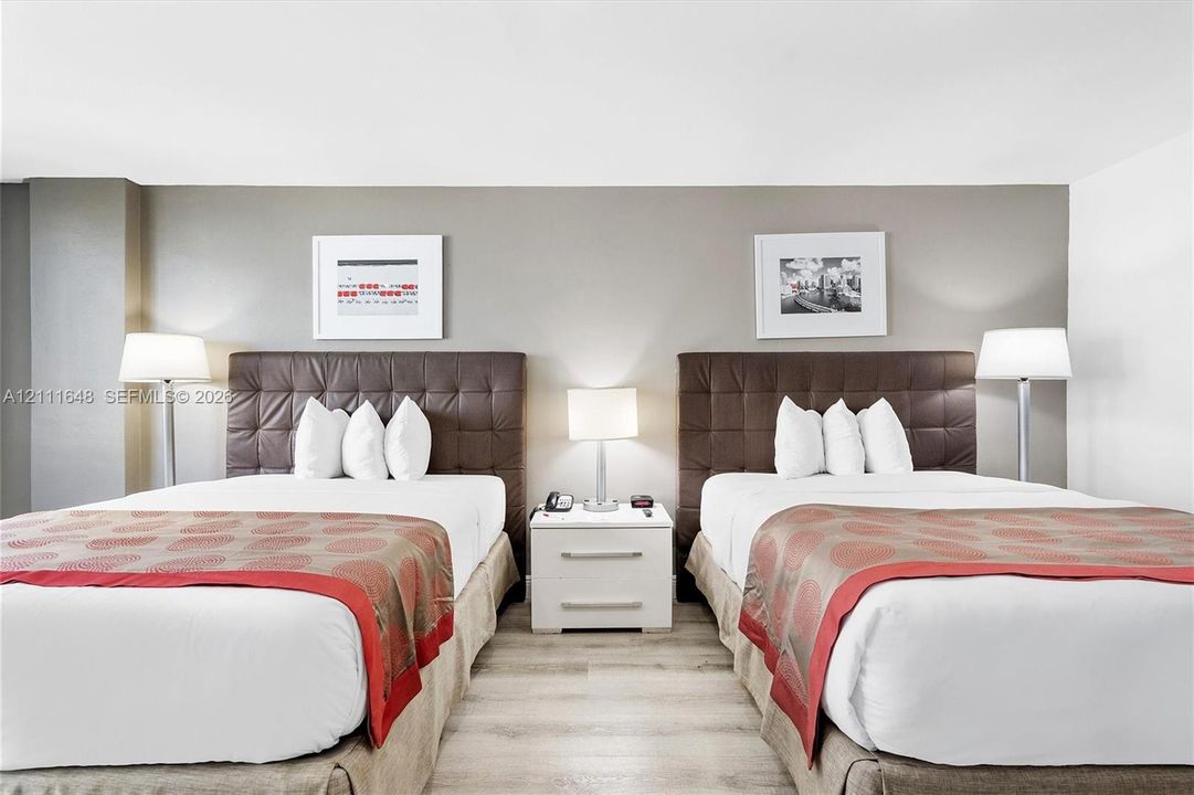 Light-toned wood-finish flooring and a central white two-drawer nightstand with a metallic finish hardware
