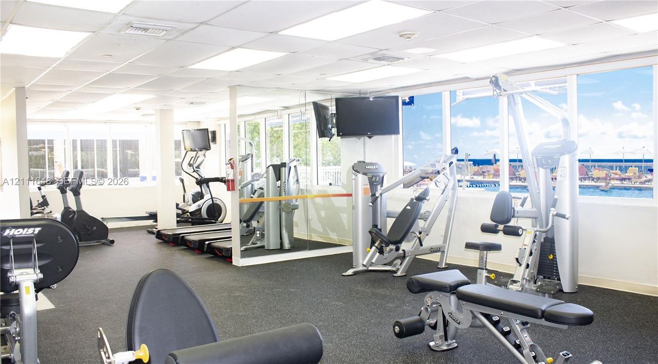 Fitness center featuring rubber flooring, expansive floor-to-ceiling windows, mirror-paneled walls, and recessed grid lighting