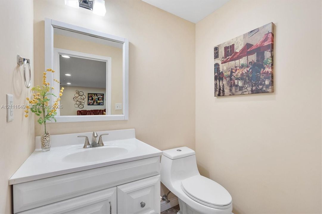White vanity cabinet with an integrated sink, solid-surface countertop, metal faucet, framed wall mirror, and dual-flush toilet