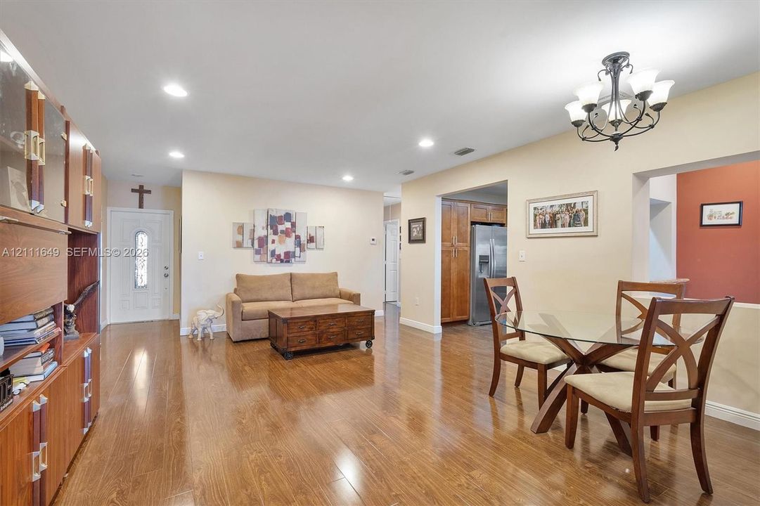Open-concept living space featuring wood-finish flooring, recessed lighting, a decorative multi-arm chandelier, and built-in floor-to-ceiling cabinetry
