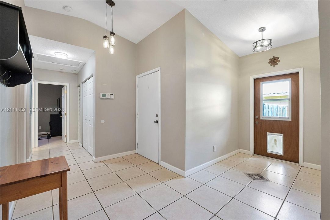 Foyer featuring ceramic tile flooring, vaulted ceilings, multi-light pendant lighting, a glass-panel entry door, and a built-in wall shelf