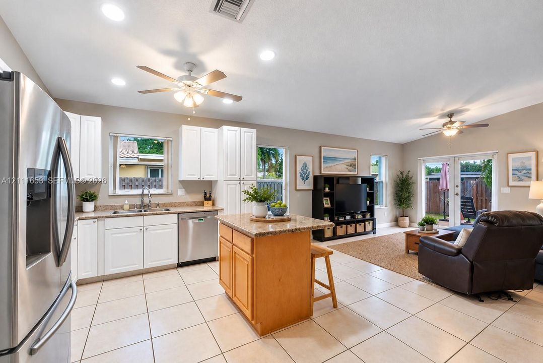 Open-concept kitchen featuring white cabinetry, stone-finish countertops, stainless steel appliances, a center island with wood cabinetry, and neutral-tone tile flooring